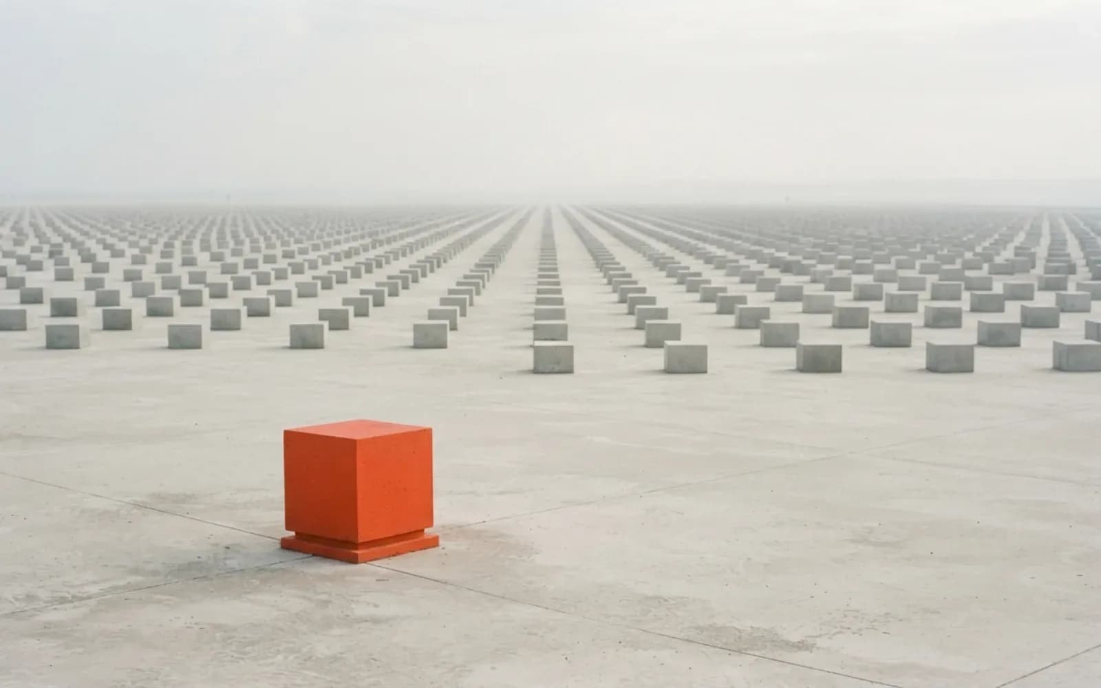A single orange cube on a vast plain of identical grey blocks