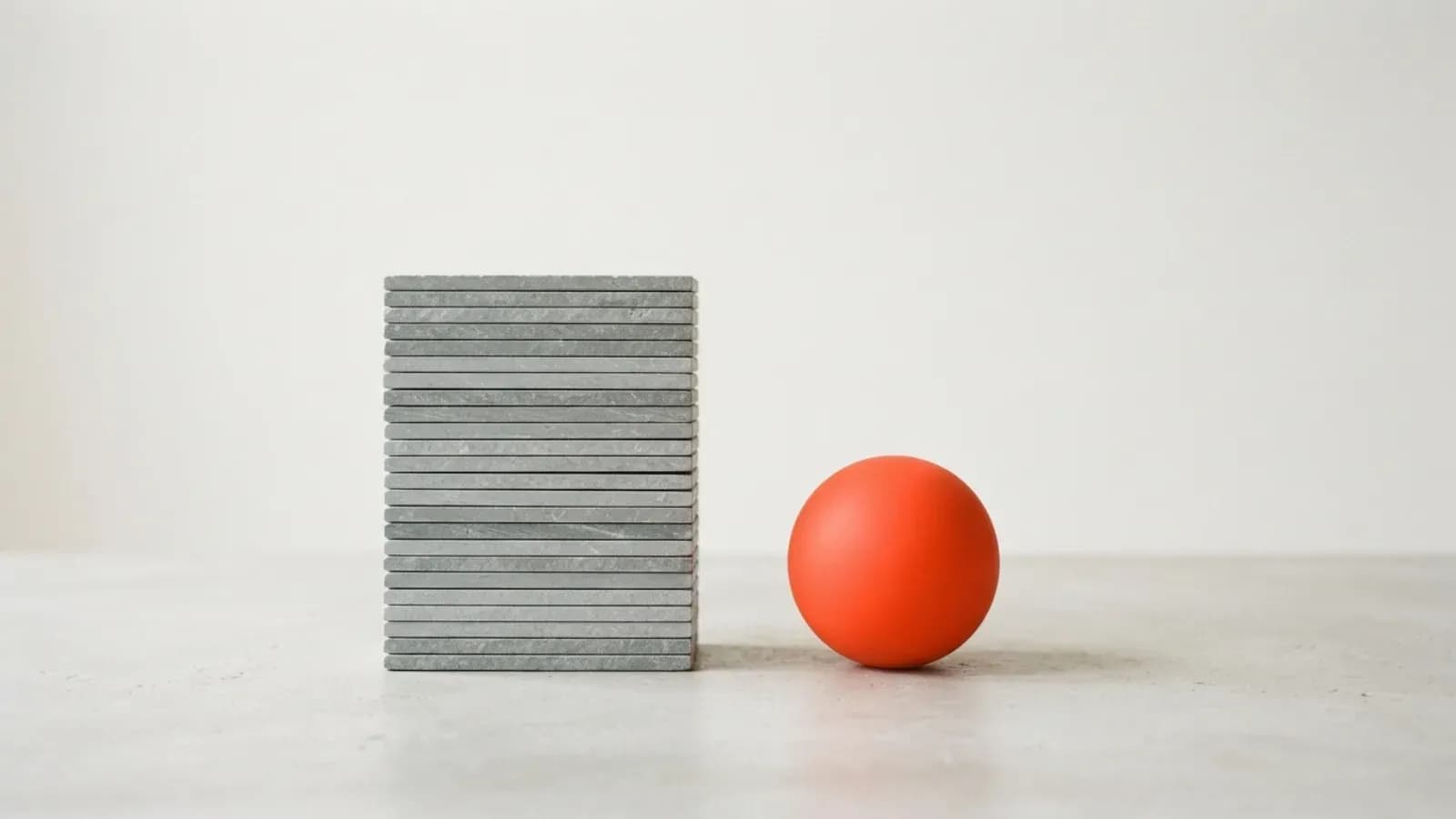 A tall stack of grey slabs beside one orange sphere